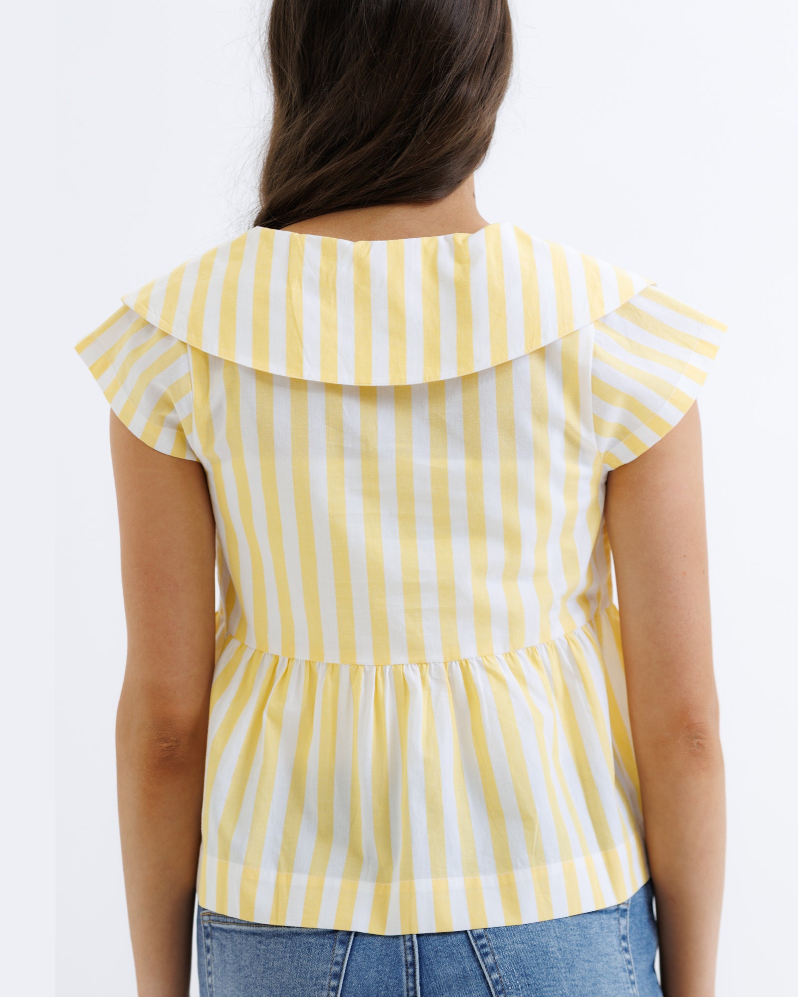 Yellow and white striped top worn by a person on a plain background