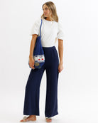 Woman wearing a white top and navy pants holding a blue bag on a white background