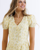 Woman wearing a yellow floral dress against a white background