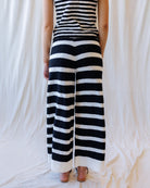 A person shown from the back wearing a sleeveless black and white horizontally striped top and matching wide-leg pants, standing against a draped white fabric backdrop.