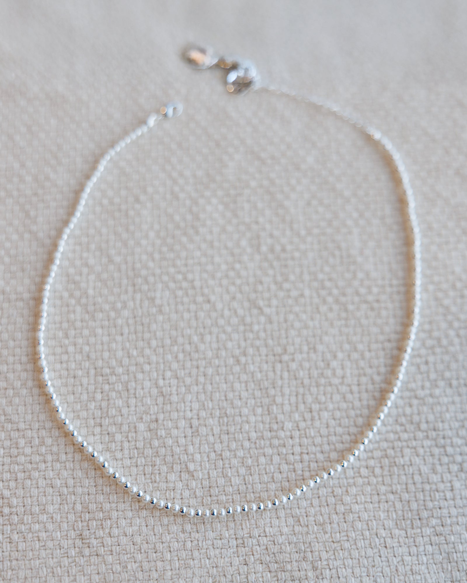 Silver necklace on a beige textured fabric background