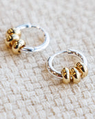 Pair of gold and silver hoop earrings on a textured beige surface