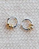 Pair of gold and silver hoop earrings on a textured beige fabric background