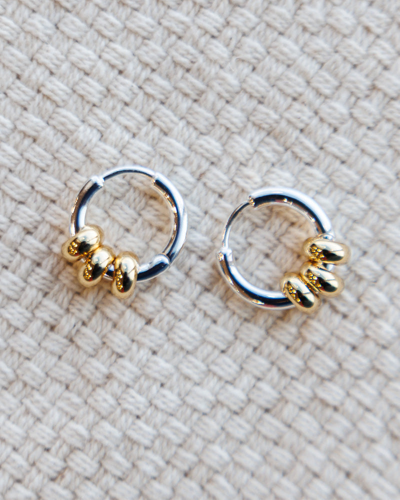 Pair of gold and silver hoop earrings on a textured beige fabric background