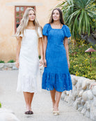 Two women in dresses standing outdoors with a garden and building in the background