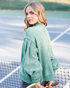 A woman on a tennis court wearing a sage green knit sweater, holding a tennis racket.