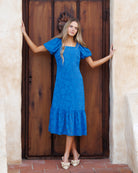 Woman in a blue dress standing in front of a wooden door.