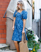 Woman in a blue dress holding a straw bag outdoors.