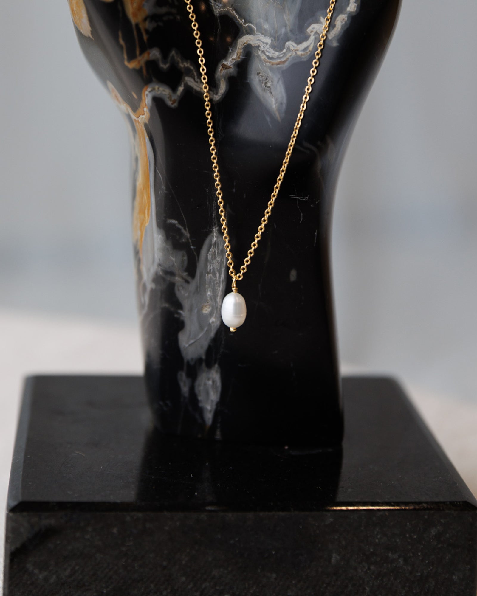 Gold necklace with a pearl pendant on a black mannequin bust.