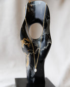 Gold necklace with a pendant on a black marble stand against a white background