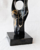 Gold necklace with a butterfly pendant on a black marble stand against a white background