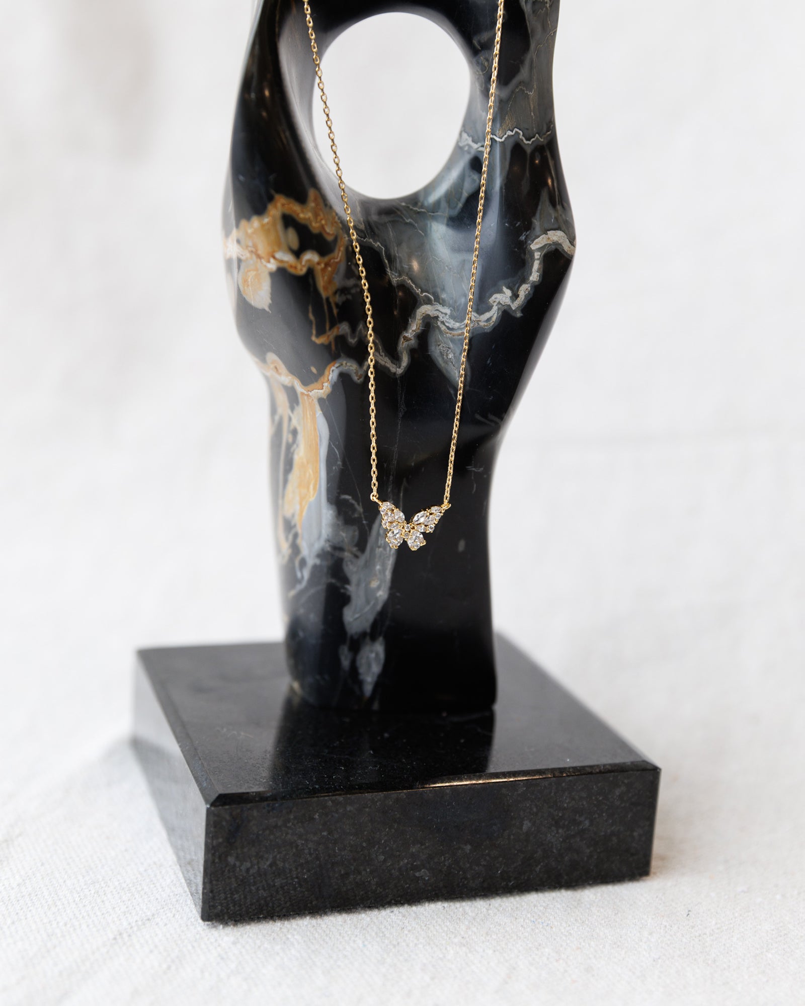 Gold necklace with a butterfly pendant on a black marble stand against a white background