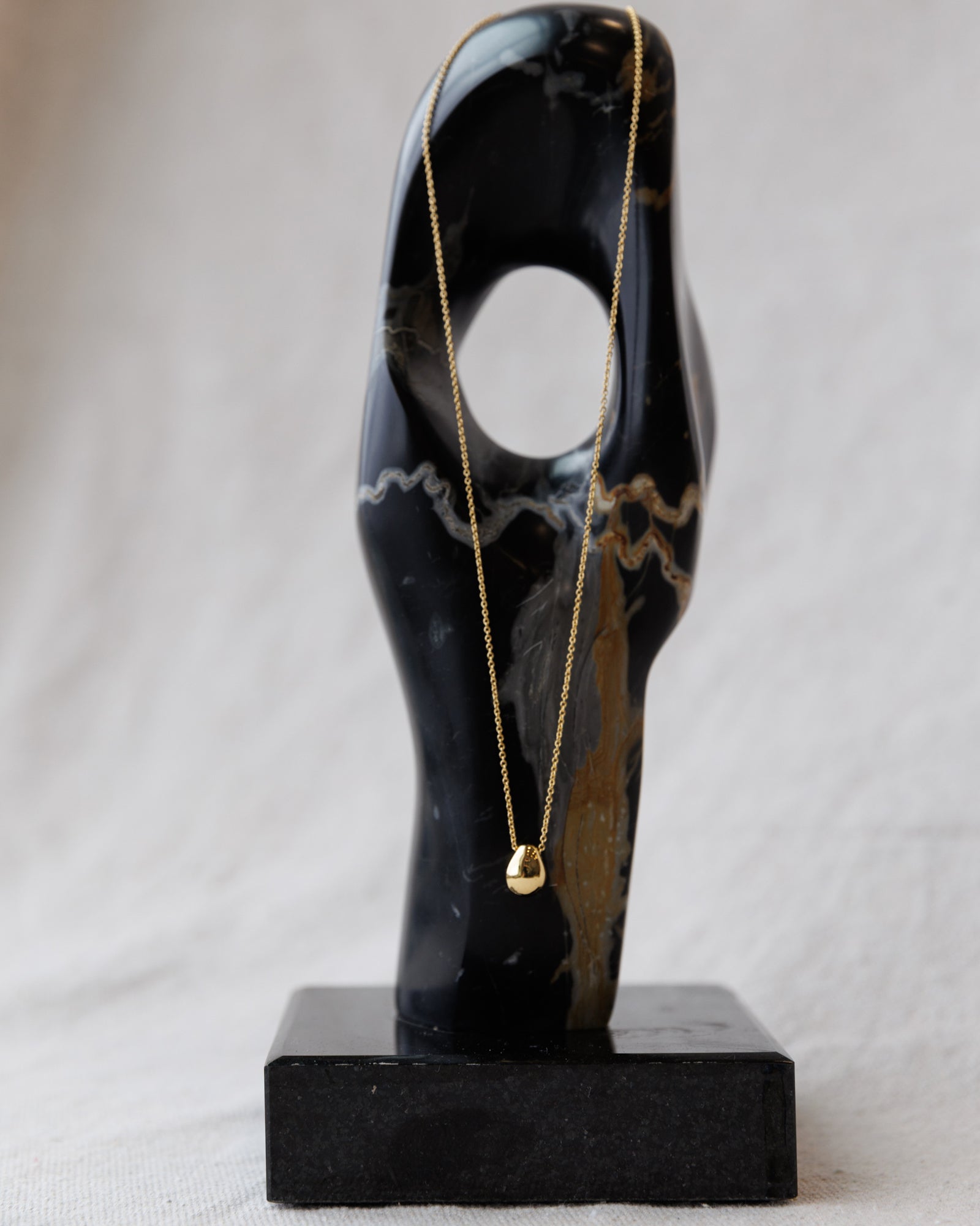 Gold necklace on a black marble bust against a gray background