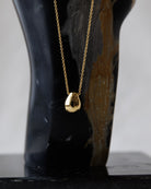 Gold necklace with a pendant on a black mannequin against a white background