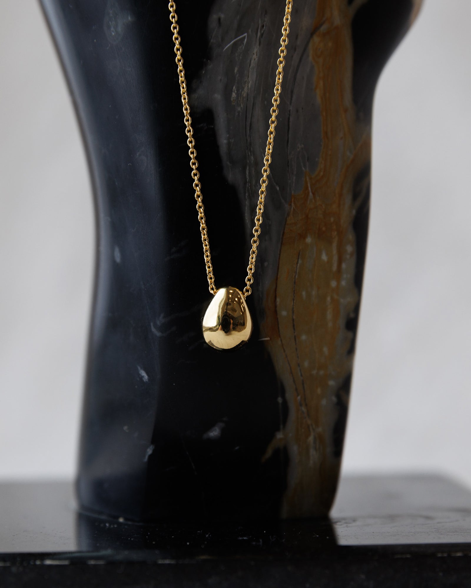 Gold necklace with a pendant on a black mannequin against a white background