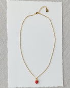 Gold necklace with a red heart pendant on a white card