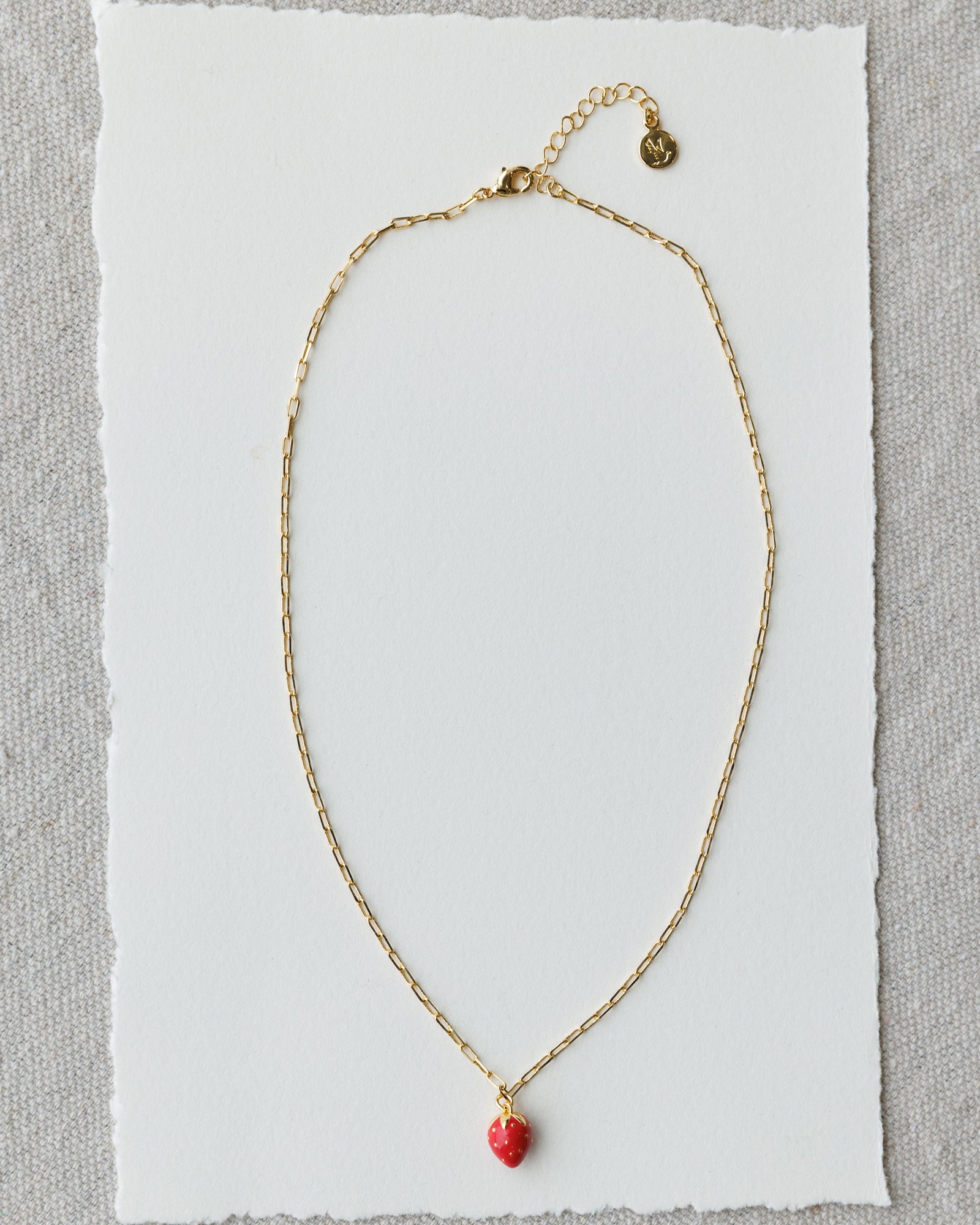 Gold necklace with a red heart pendant on a white card