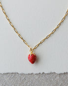 Gold necklace with a red strawberry pendant on a light gray background