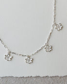 Silver necklace with flower pendants on a light gray background