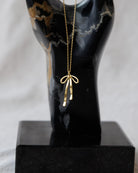 Gold necklace with a bow pendant on a black mannequin bust against a white background