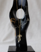 Gold necklace with a bow pendant on a black marble bust against a white background