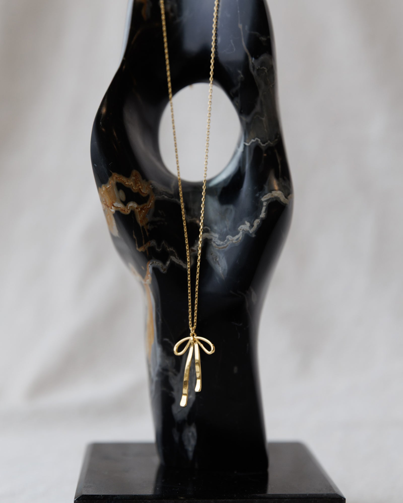 Gold necklace with a bow pendant on a black marble bust against a white background