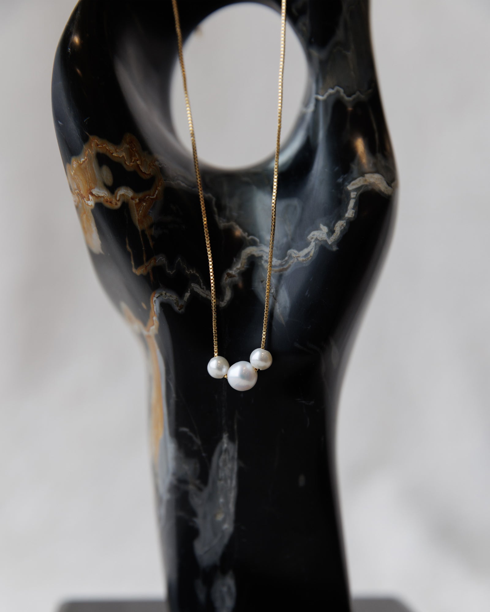 Pearl necklace on a black marble stand with a white background