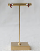 Gold earring stand with red and clear earrings on a light gray background