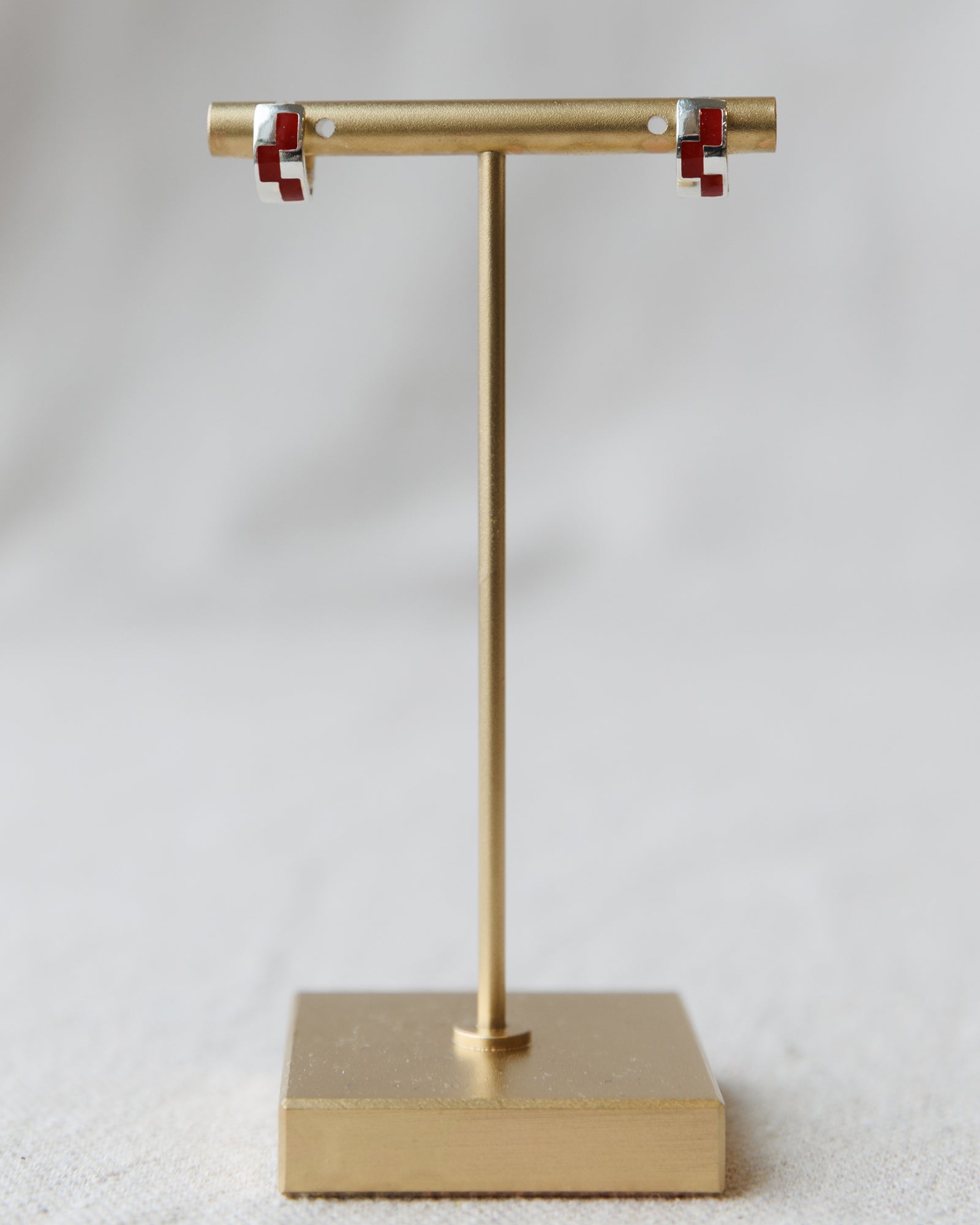 Gold earring stand with red and clear earrings on a light gray background
