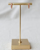 Gold T-shaped jewelry stand with pink earrings on a light gray background