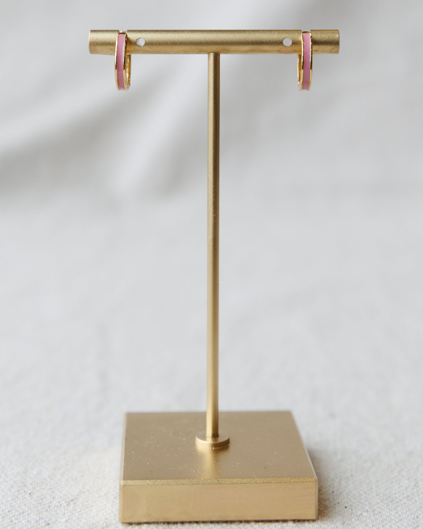 Gold T-shaped jewelry stand with pink earrings on a light gray background