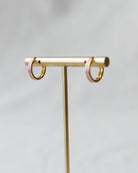 Gold hoop earrings on a gold stand against a light gray background