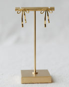 Gold earring stand with bow-shaped earrings on a light gray background
