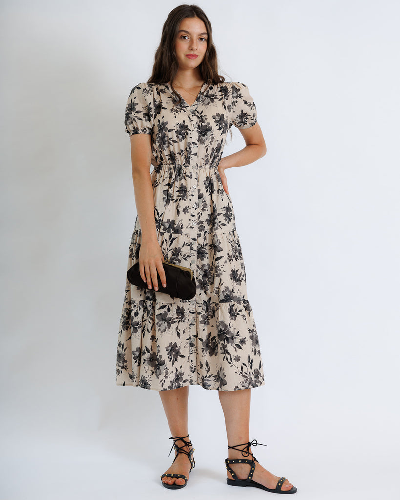 Woman wearing a floral dress holding a clutch against a white background