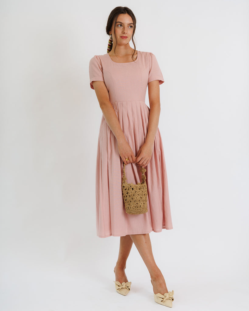 Woman wearing a pink dress holding a patterned handbag on a white background