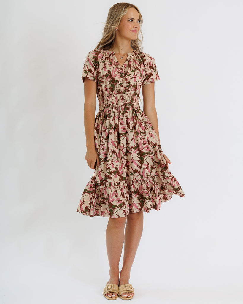 Woman wearing a brown and pink floral print short sleeve knee length dress on a white background