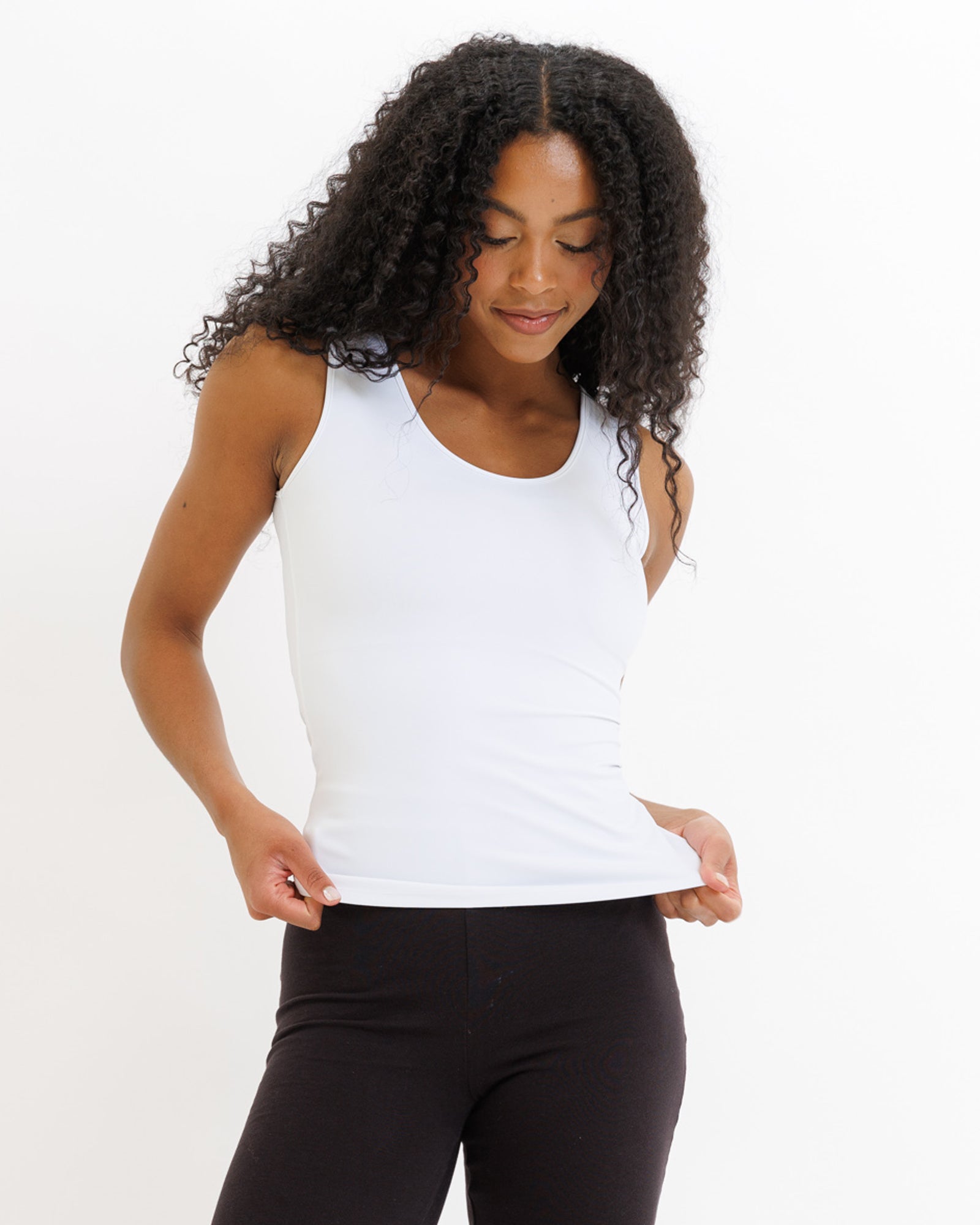 Woman wearing a white tank top and black leggings on a white background