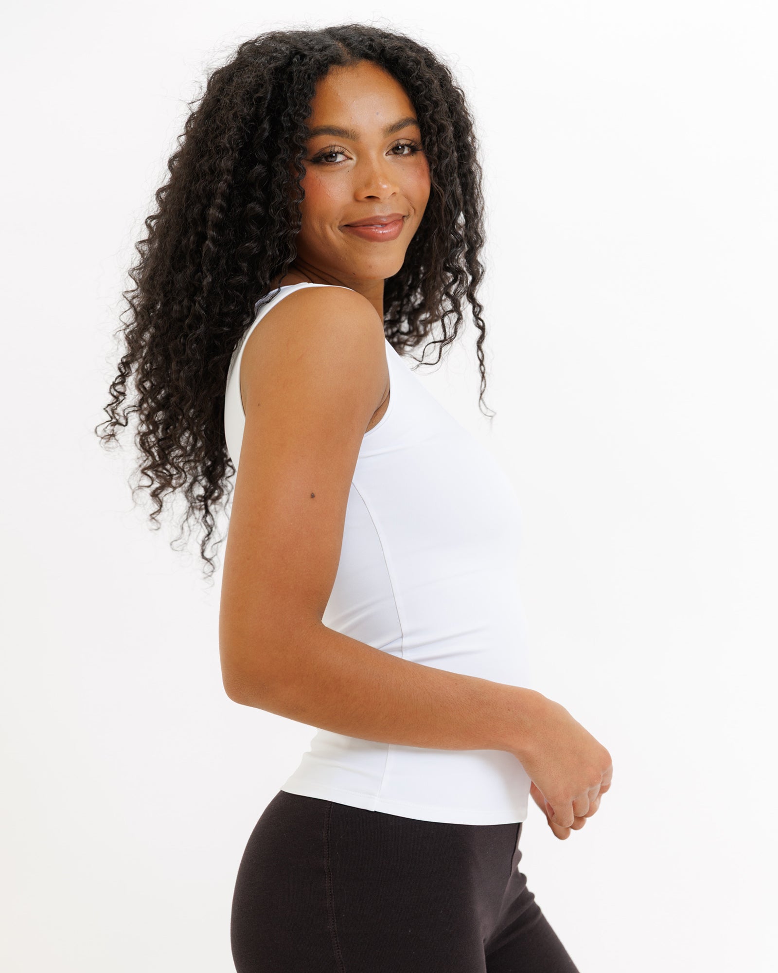 Woman wearing a white tank top and black pants on a white background