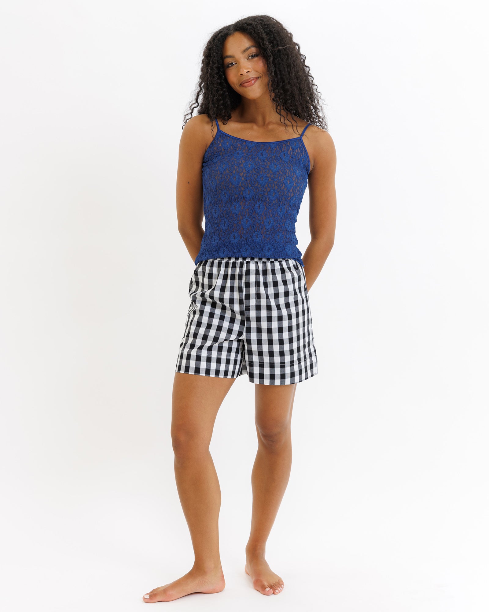 Woman wearing a blue lace top and black and white checkered shorts on a white background