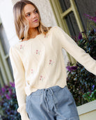 Woman wearing a cream-colored cardigan with floral embroidery, standing outdoors.