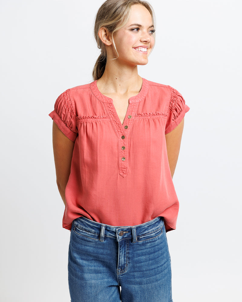 Model wearing a burnt orange short sleeve v-neck with buttons down front placket blouse