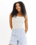 Woman wearing a yellow lace top and blue striped shorts on a white background
