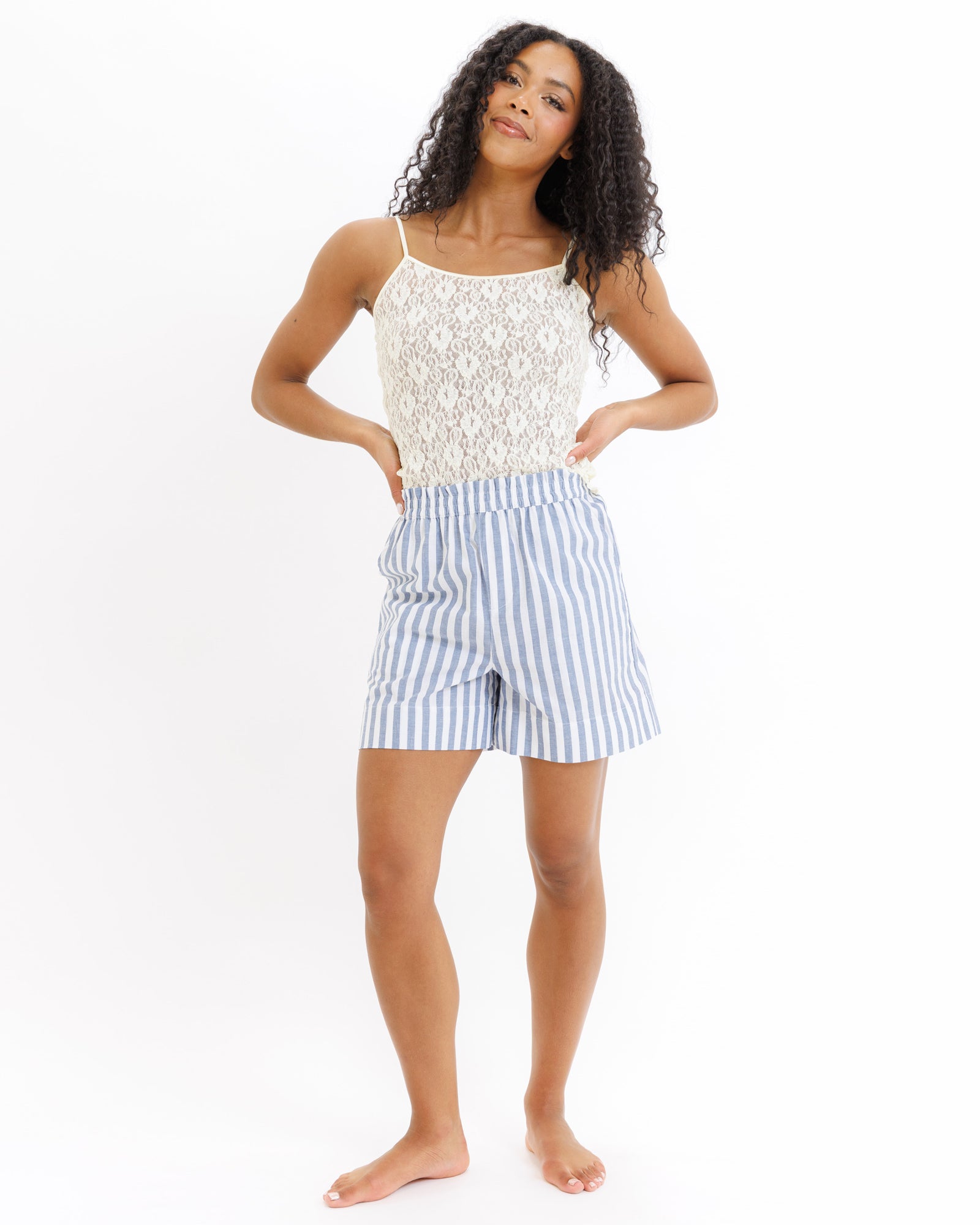 Woman wearing a yellow lace top and blue striped shorts on a white background
