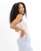 Woman wearing a yellow lace top and blue striped pants on a white background