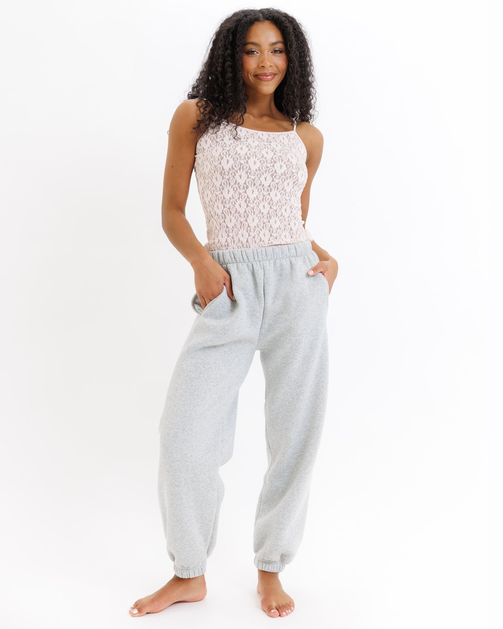 Woman wearing a pink lace top and gray sweatpants on a white background