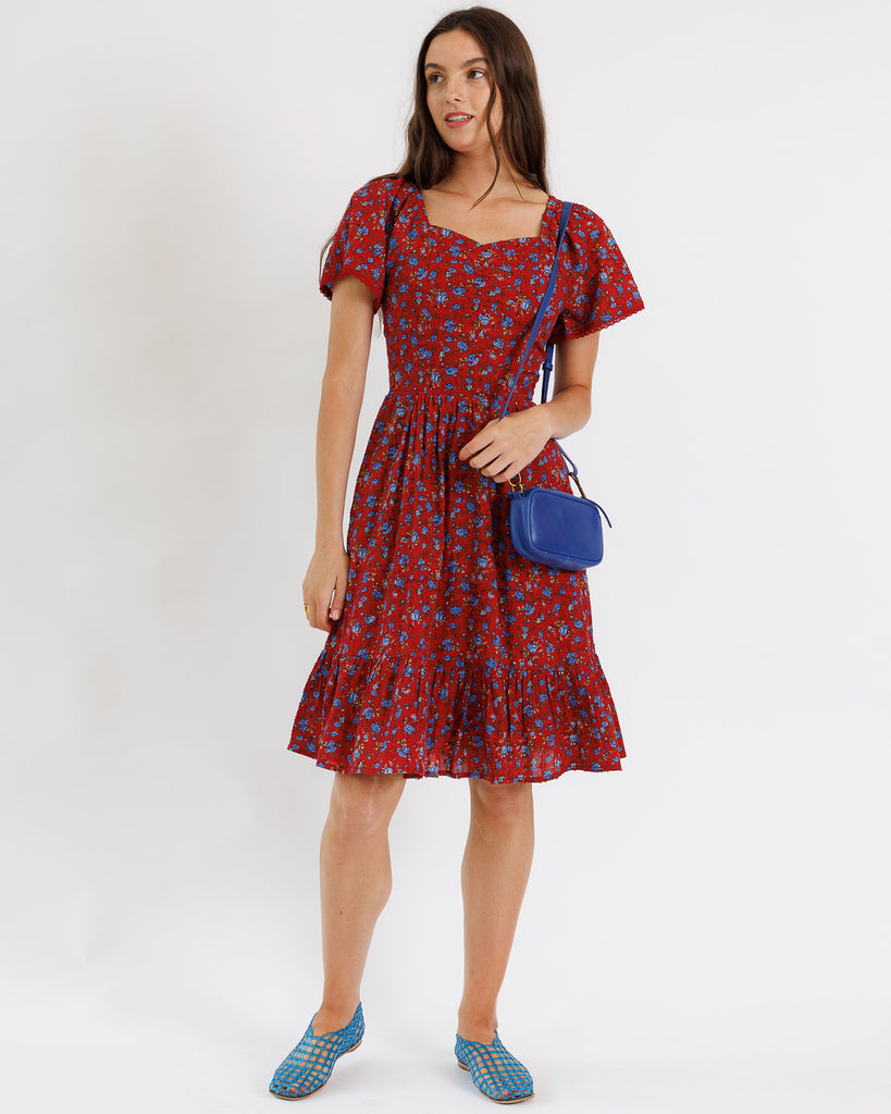 Woman wearing a red floral dress with a blue bag on a white background