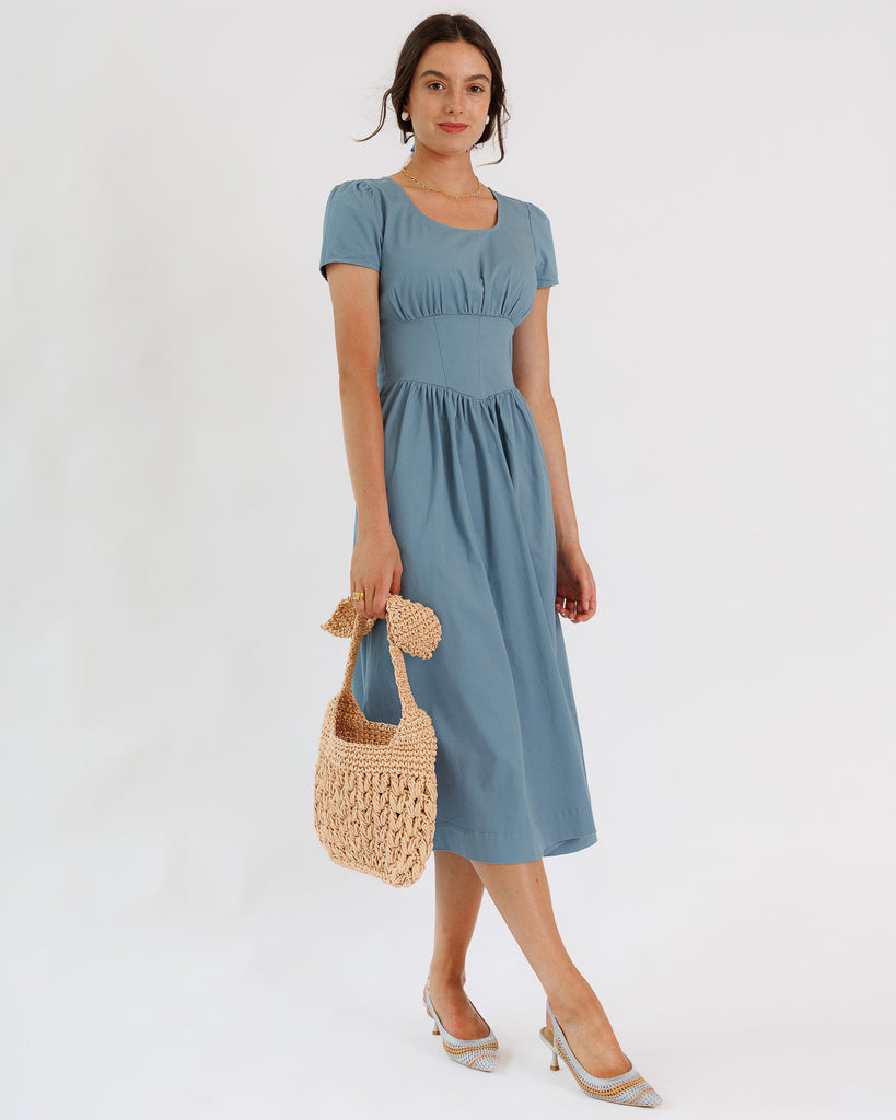 Woman wearing a blue dress holding a woven bag on a white background