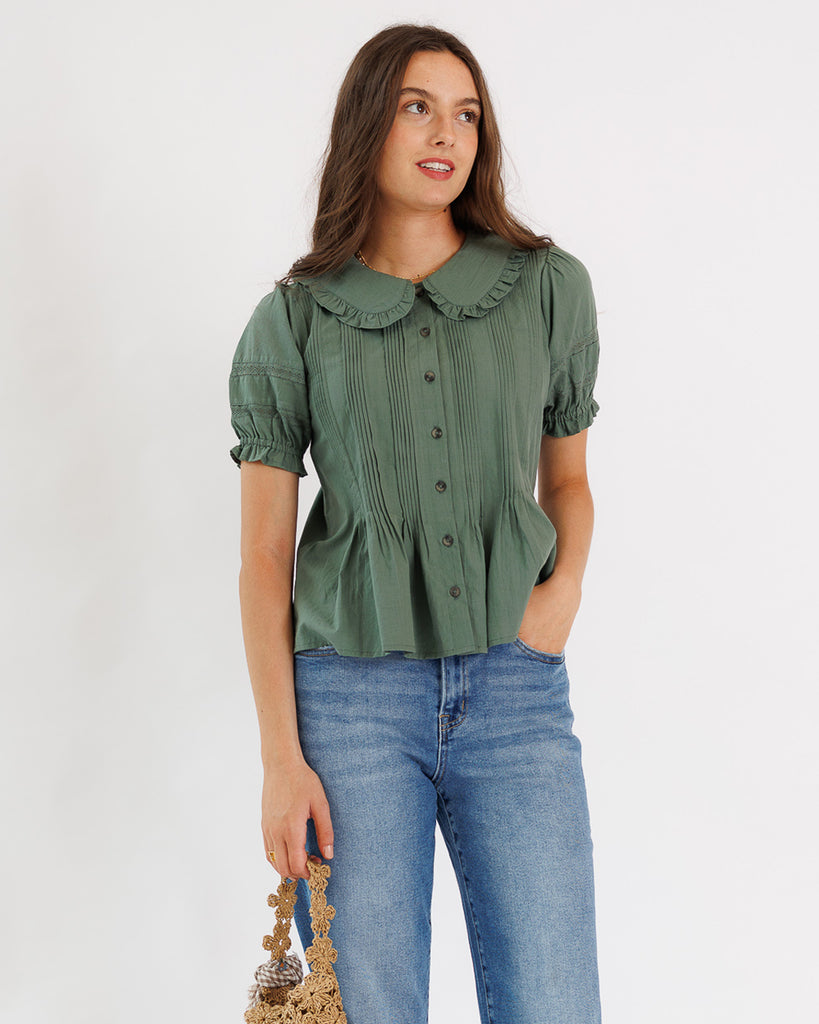 Woman wearing a green blouse with a ruffled collar and blue jeans on a white background