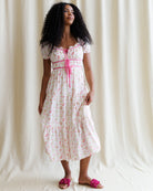 Woman wearing a white floral dress with a pink ribbon against a plain background