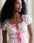 Woman wearing a floral dress with pink accents, standing against a neutral background